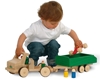 Un petit garçon joue avec un camion en bois, modèle de base long auquel est attaché une remoque verte.