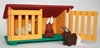 Red, green and yellow toy farm rabbit cage with one of the two  doors open, a small light brown wool rabbit in the cage, a dark brown rabbit in front of the cage.
