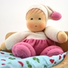 De knuffelpop in roze en witte badstof zit in een bedje met blauw donsdeken.