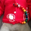 Le ventre d'un bébé au pull rouge auquel est attaché la chaîne à sucette aux perles de bois multicolores.