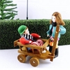 Popje voor poppenhuis, jongen met rode dikke trui zit in een houten kar die zijn poppenhuis zusje voortsleept.