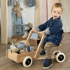 Un petit garçon vêtu de bleu est assis sur un vélo cargo en bois et transporte ses jouets dans le coffre avant. Il est en train de faire marche arrière.marche arrière.