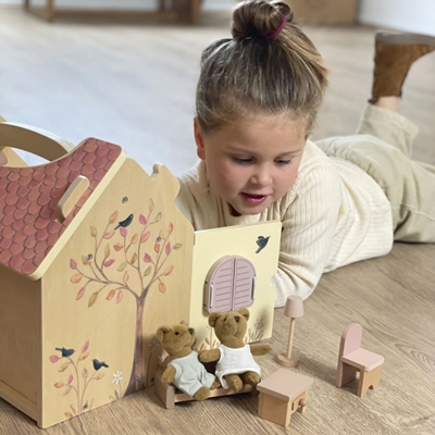 A little girl plays with the bears and their furniture inside and outside the wooden dollhouse.