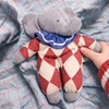 Doudou éléphant Nanchen avec vêtements de cirque: tenue à losanges rouge et blanc cassé et collerette bleue, tenu par une main d'enfant.