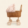 Rieten poppenwagen met zacht roze bekleding bedrukt met kleine paddestoelen.