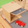 Une petite voiture en bois rouge quitte le double box garage jouet en bois dont la porte est ouverte et l'intérieur avec plateau intermédiaire visible.