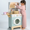 Une fillette joue avec la machine à laver jouet bleue clair, planche et fer à repasser, étendoir, panier à linge et produits lessive.
